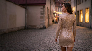 Woman in a champagne sequin long sleeve mini dress walking down a cobbled street at dusk